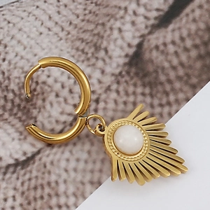 Macro shot of boho gold sunburst drop earring with white gemstone on textured surface
