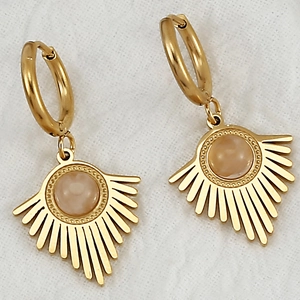Macro detail of gold-plated geometric earrings featuring central inlaid stone and sunburst rays