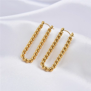 Macro shot of gold-plated twisted rectangular earrings on white silk fabric