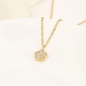 Elegante collana dorata con ciondolo floreale e cristalli scintillanti su ceramica