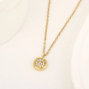 Dettaglio ravvicinato di una collana con ciondolo tondo dorato con micro-pavé di zirconi