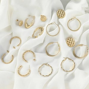 Collection of luxury gold geometric twisted hoop earrings and pearl studs on white silk fabric