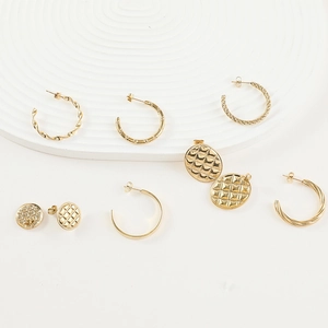 Détail de bijoux en titane doré avec créoles torsadées et clous d'oreilles texturés