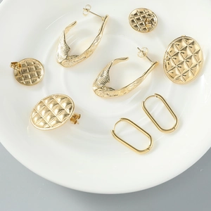 Détail de boucles d'oreilles en acier titane doré avec motifs matelassés sur plateau blanc
