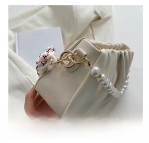 Close-up of cream pleated shoulder bag with pearl strap, gold ring and floral scarf