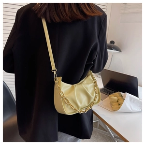Detail of a beige pleated dumpling bag with a gold chain strap worn as a shoulder bag