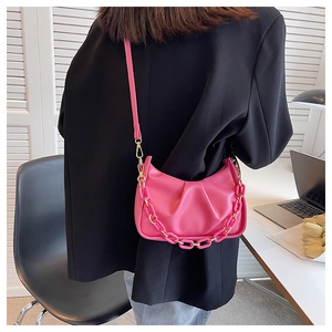 Detail of fuchsia pleated shoulder bag with resin chain worn over black blazer