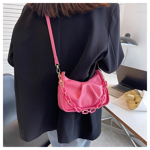 Detail of fuchsia pleated croissant bag with acrylic chain and crossbody strap shown on a desk