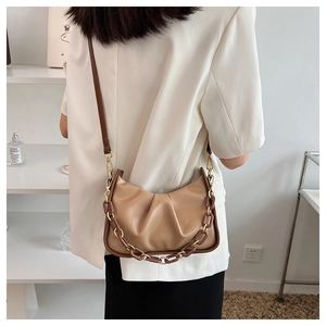 Detail of khaki pleated cloud bag with acrylic chain strap on model in modern setting
