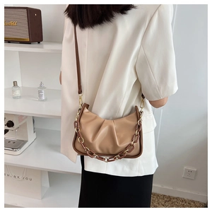 Detail view of a beige ruched cloud bag with stylish brown chain and slim strap