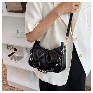 Detail of black pleated cloud bag with golden chain strap on a white blazer outfit