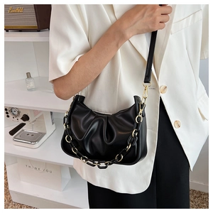 Detail of black pleated cloud bag with gold chain strap on a minimalist studio backdrop