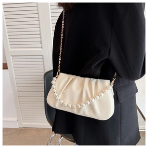 Detail of off-white ruched bag with pearl strap and golden chain on model's side