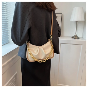 Detail of a creamy white pleated cloud bag featuring a chunky gold acrylic chain and leather strap