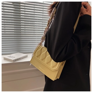 Detail of yellow embossed crossbody bag with vertical wave texture and silk scarf strap