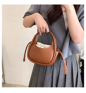 Sac à main demi-lune en cuir marron avec doublure à cordon crème tenu par un modèle