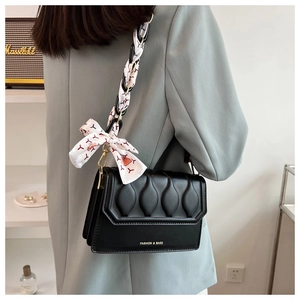 Detail of black quilted shoulder bag with chain strap and elegant silk scarf handle