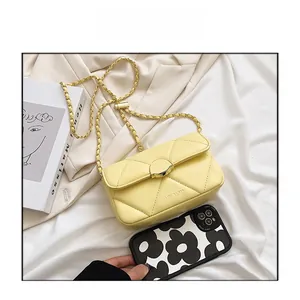 Détail du sac bandoulière jaune matelassé avec fermoir doré sur tissu blanc moelleux