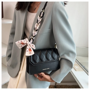 Detail of black crossbody bag with wave quilting and silk scarf chain strap on model