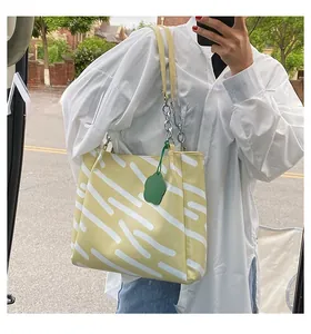Close-up of yellow tote bag with white abstract patterns and a green flower charm