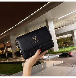 Detail of black quilted leather shoulder bag featuring a gold deer logo and chain strap