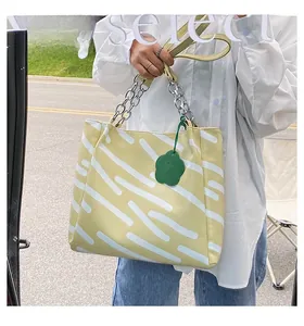 Detail of yellow tote bag with abstract white stripes, metal chain, and floral charm