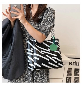 Detail of black and white striped tote bag with green charm and metal chain strap