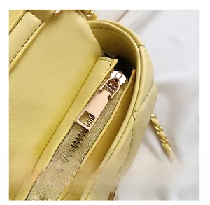 Détail du zip en métal doré et de la bandoulière en chaîne tressée de cuir sur un sac jaune