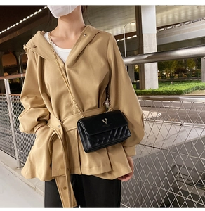 Close-up of black quilted leather crossbody bag with gold chain strap on a trench coat