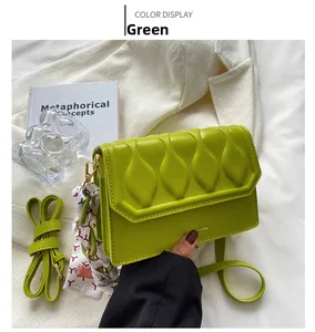 Close-up of green embossed small square bag with decorative silk scarf and strap