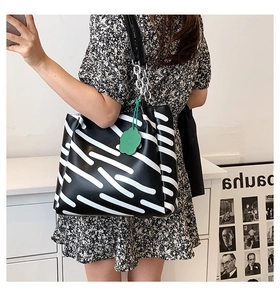 Detail of black and white striped tote bag with green cloud charm and chain strap