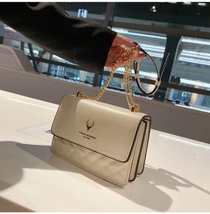 Detail of beige quilted shoulder bag with golden deer logo and accordion side panels
