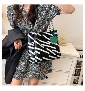 Detail of abstract black and white striped tote bag with silver chain and green charm