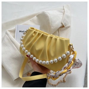 Detail of yellow pleated cloud bag featuring pearl handle and silk scarf chain strap