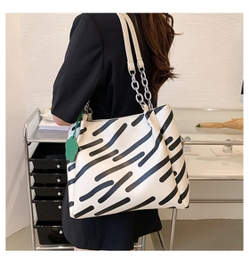 Detail of off-white tote bag with black stripes, chain strap and green floral charm