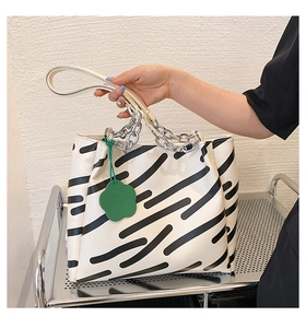 Detail of striped tote bag with silver chain and green flower charm on cream strap