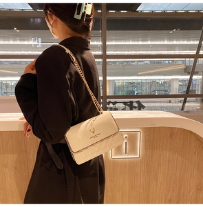 Close-up of cream quilted shoulder bag with golden deer logo and chain strap detail
