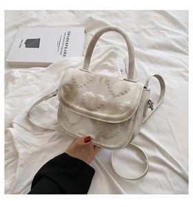 Détail du sac selle beige avec texture gaufrée en forme de cœur et poignée supérieure