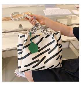 Close-up of white striped tote bag featuring silver chain handle and green flower charm