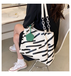 Detail of striped tote bag featuring metal chain strap and green floral charm