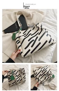 Detail of elegant white tote bag with black abstract stripes and green cloud charm decor