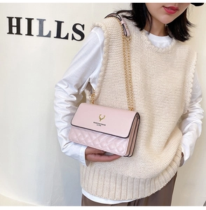 Detail of pink quilted crossbody bag featuring a gold deer logo and chain strap