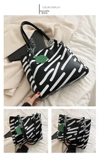 Detail of black tote bag with white capsule patterns, chain strap and green flower charm