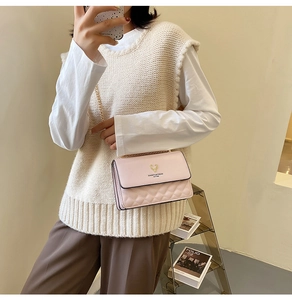 Detail of pink quilted square crossbody bag featuring a golden deer head logo and chain