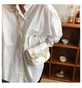 Détail d'un sac selle blanc avec texture marbrée porté par un mannequin en chemise