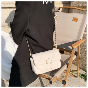 Détail d'un sac bandoulière beige matelassé avec boucle dorée et bandoulière chaîne