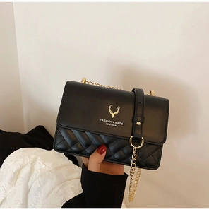 Detail of black leather crossbody bag with golden deer emblem and quilted stitching texture