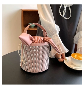 Detailed view of pink bucket bag with silver metal studs and bow decoration on a table