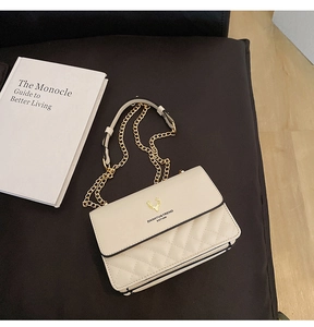 Detail of a beige quilted crossbody bag with golden deer logo and metal chain strap