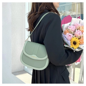 Detail of sage green saddle bag with gold logo and adjustable strap on a black blazer